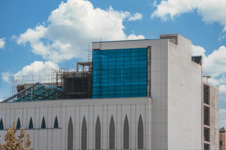 A contemporary building exterior with blue glass facade against a cloudy sky.